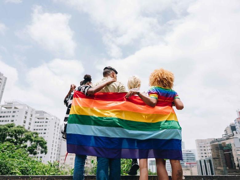 students holding a pride flag facing a city landscape